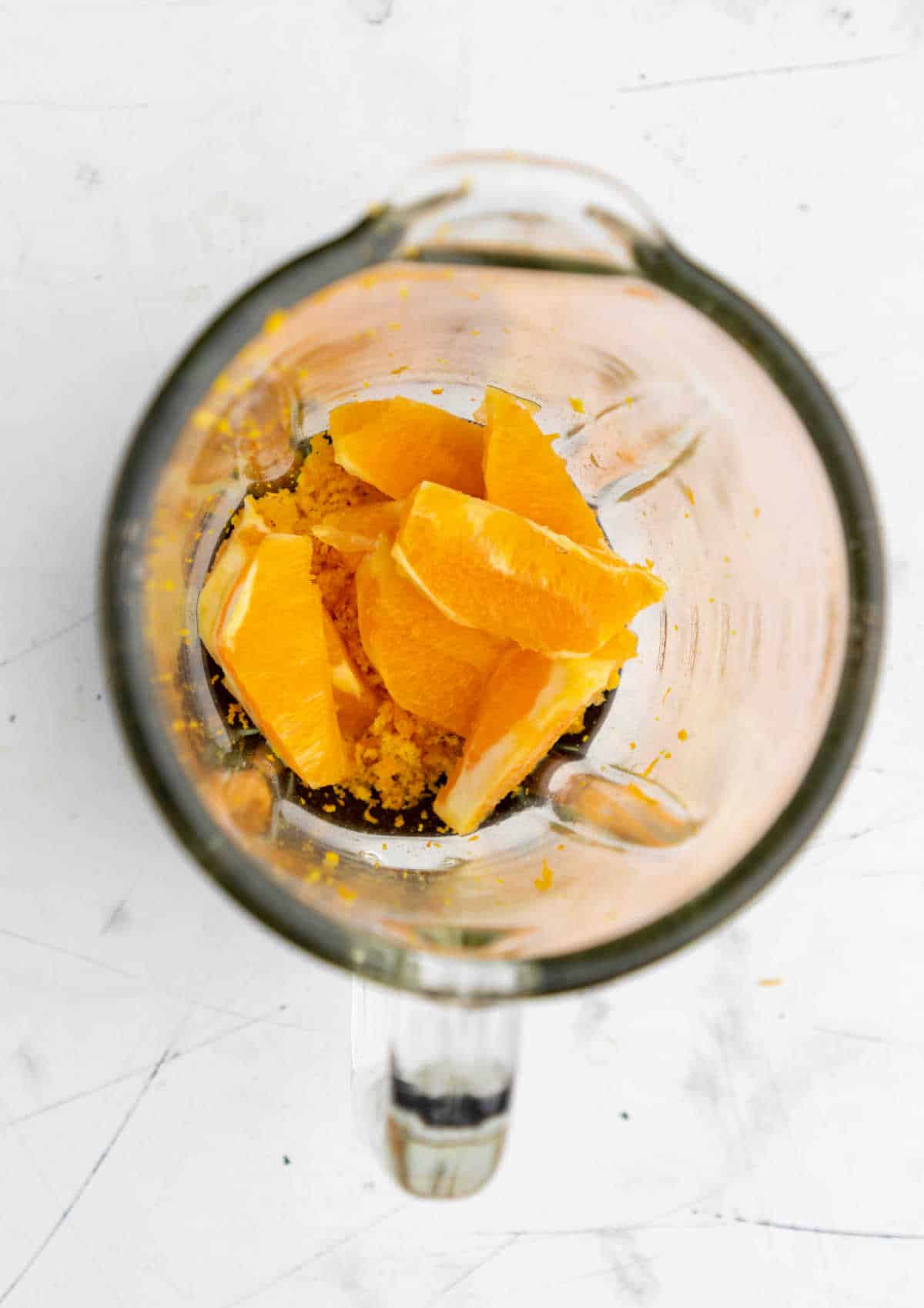 orange zest and orange sections in the bowl of blender. 