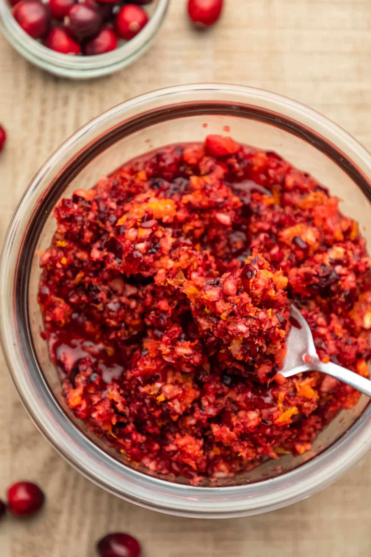 A silver spoon in a glass bowl of cranberry orange relish. 