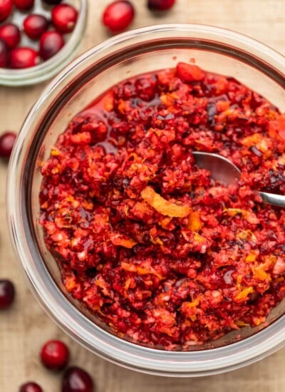 A glass dish of cranberry orange relish with a strip of orange peel on top.