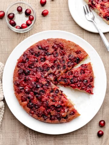A cranberry upside down cake on a white platter with a slice missing.