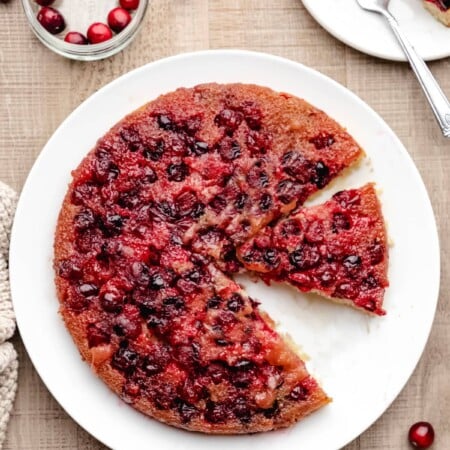 A cranberry upside down cake on a white platter with a slice missing.