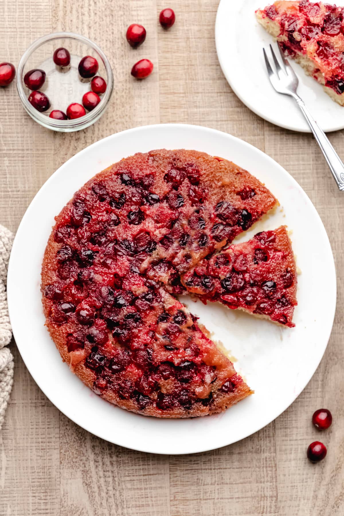 A cranberry upside down cake on a white platter with a slice missing. 