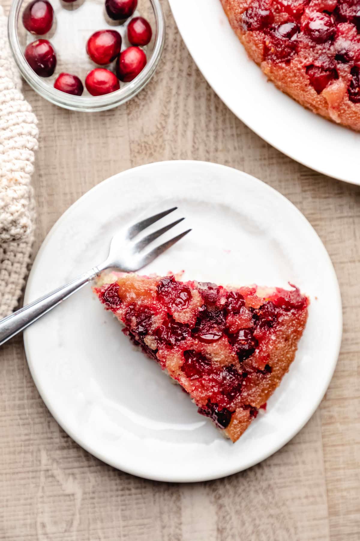 A slice of cranberry upside down cake on a white plate with a silver fork. 
