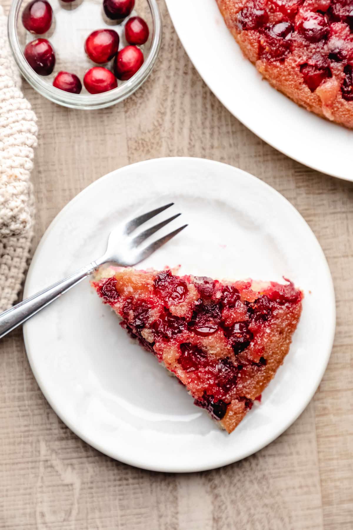A slice of cranberry upside down cake on a white plate with a silver fork.