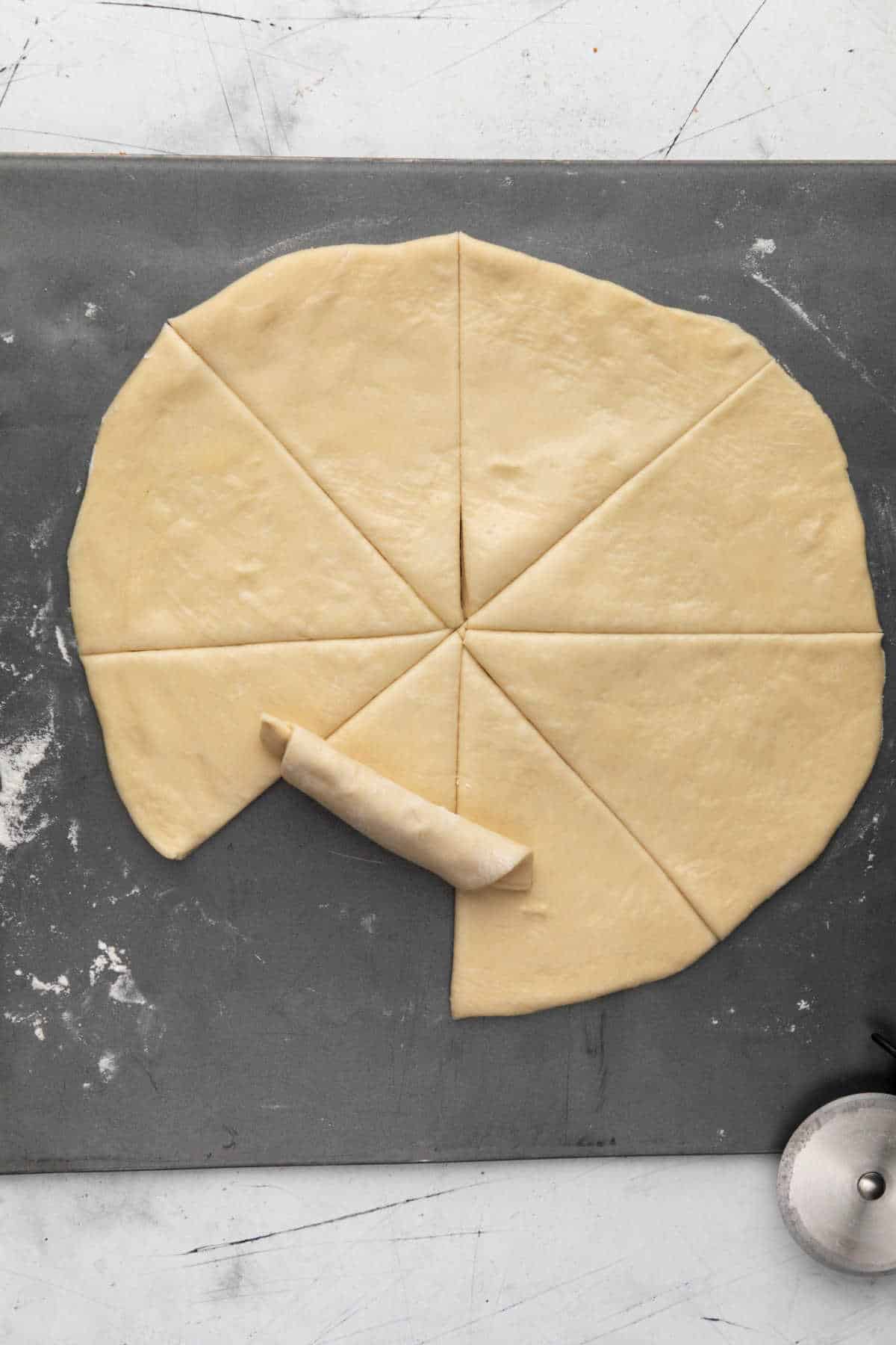 Cut crescent roll dough with a piece being rolled up. 