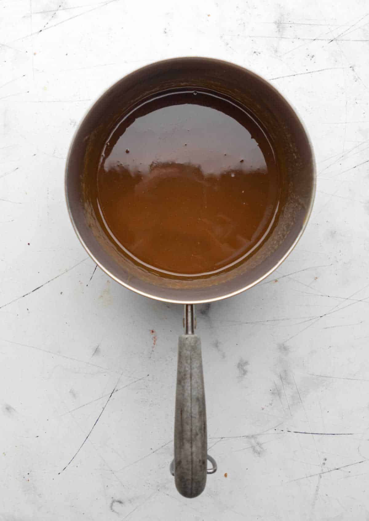 A saucepot with sticky toffee sauce in it.