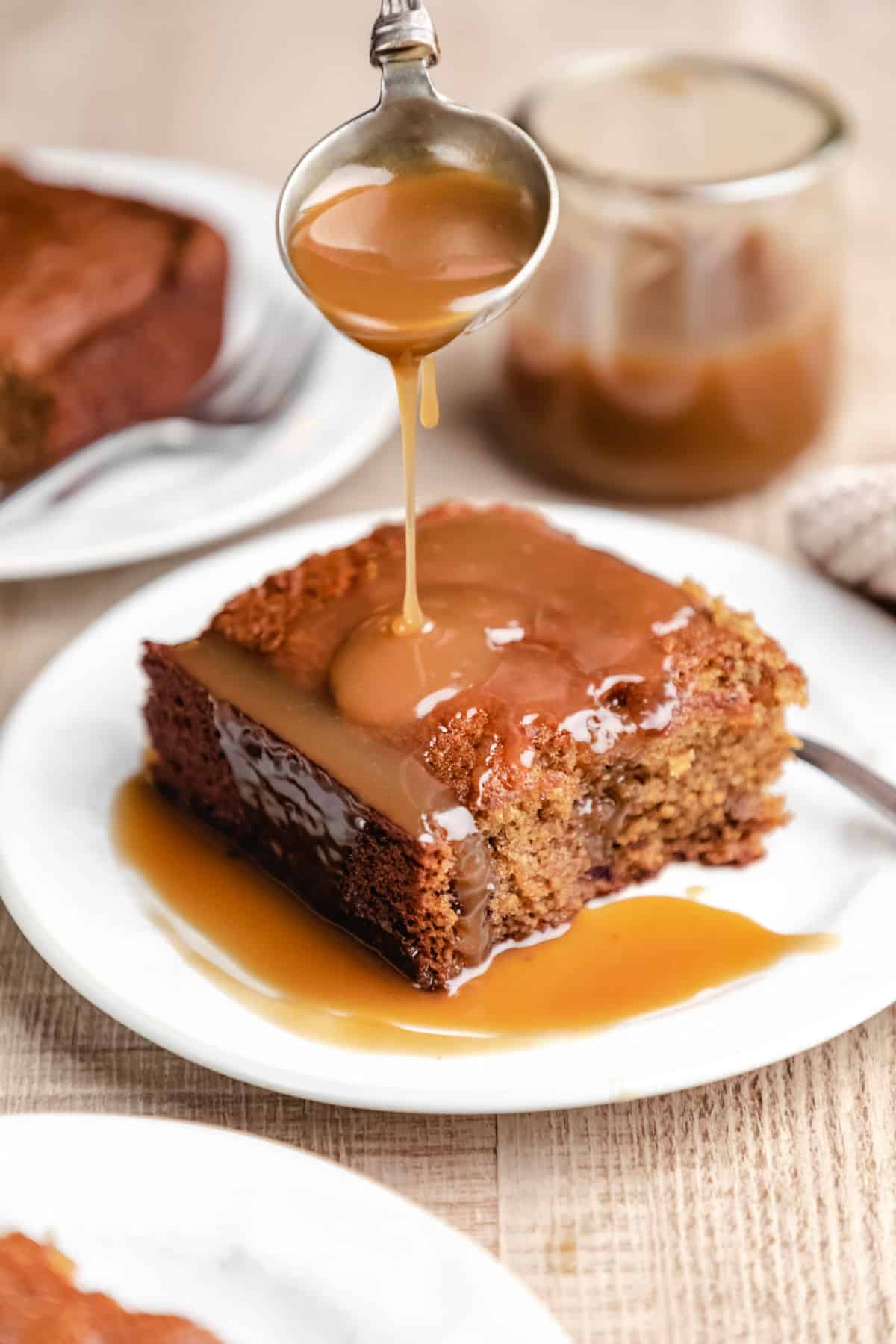 A spoon pouring sticky toffee sauce onto sticky toffee pudding cake. 