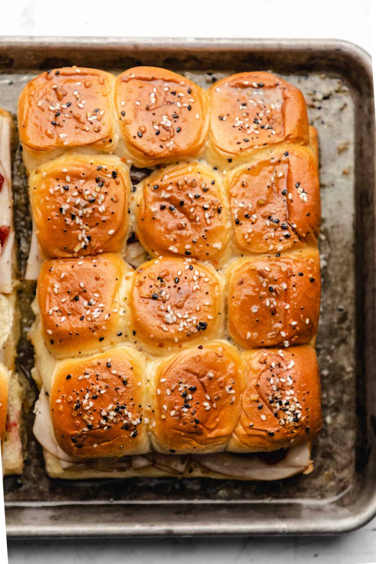 close up photo of 12 turkey and cranberry sliders on a rimmed baking sheet. 