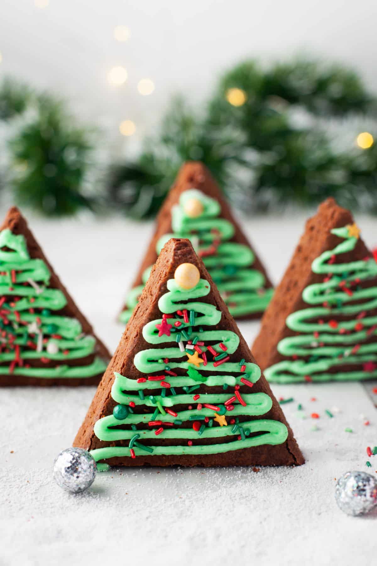 Christmas tree brownies with greenery and lights behind them. 