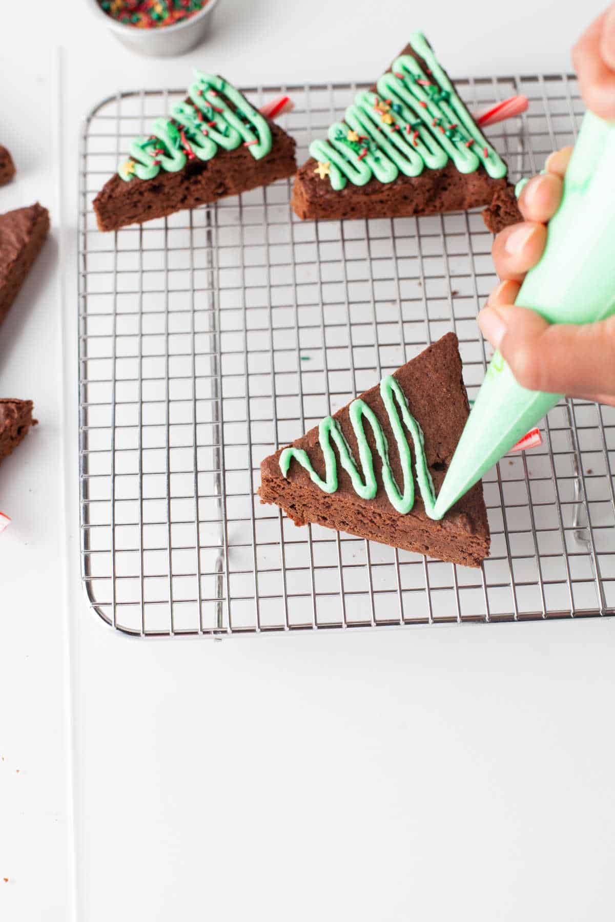 A piping bag piping green frosting onto a brownie triangle. 