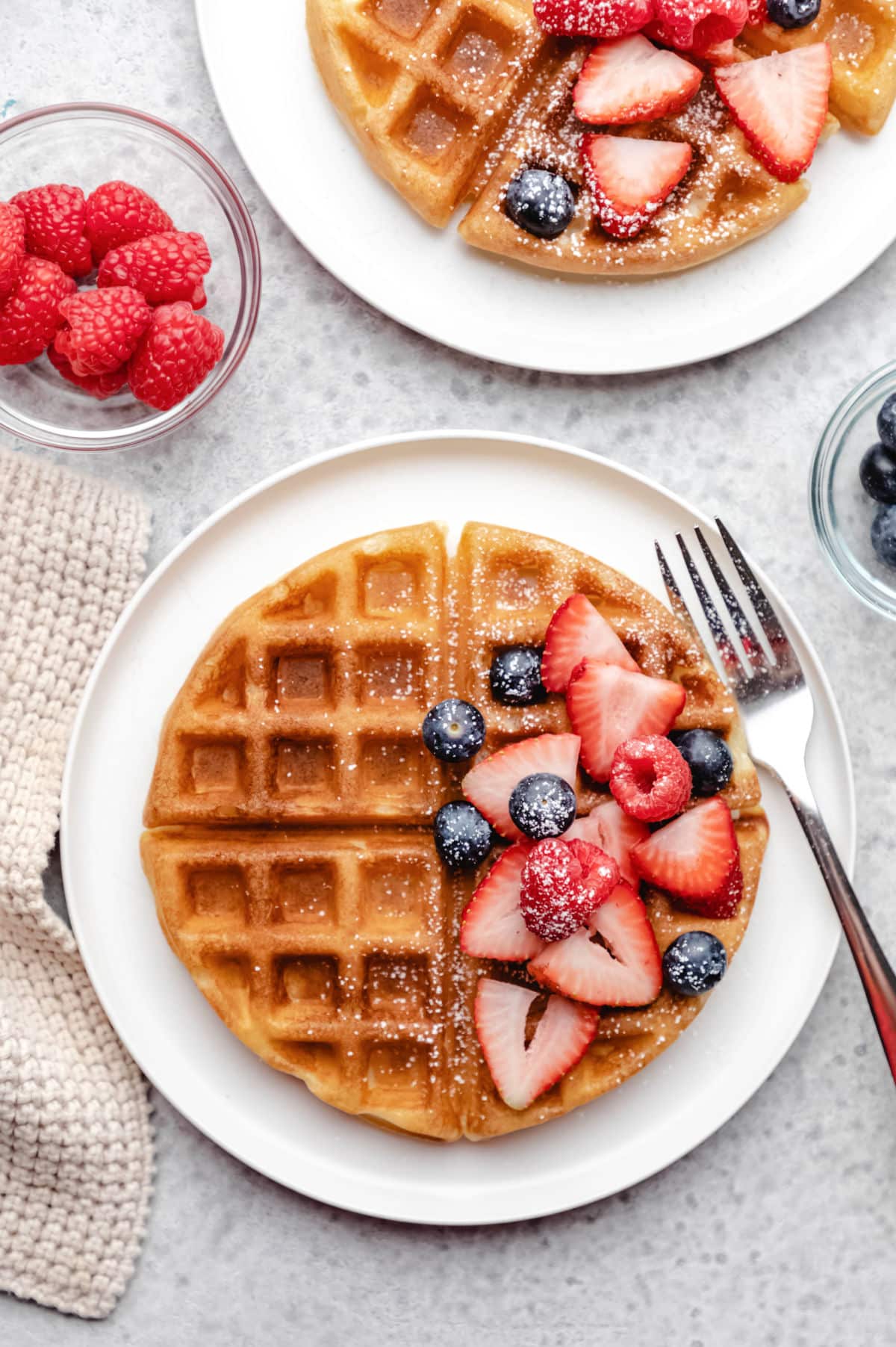 A bowl of raspberries next to two buttermilk waffles. 