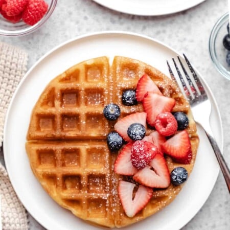 A buttermilk waffle topped with blueberries strawberries and raspberries.