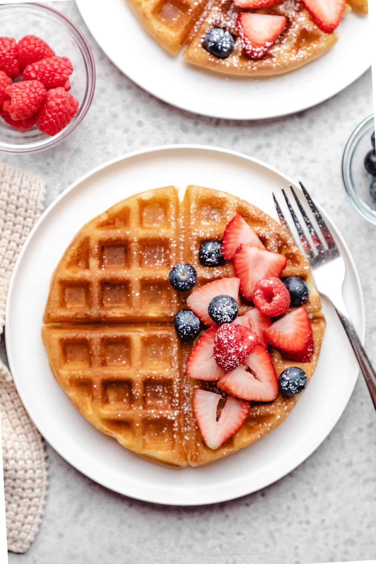 A buttermilk waffle topped with blueberries strawberries and raspberries. 