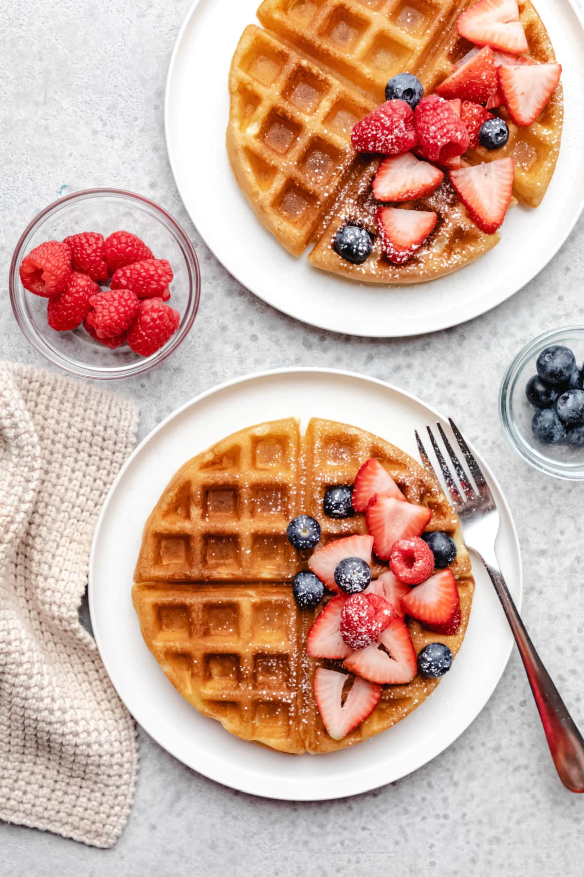 Two buttermilk waffles on white plates topped with fresh berries. 