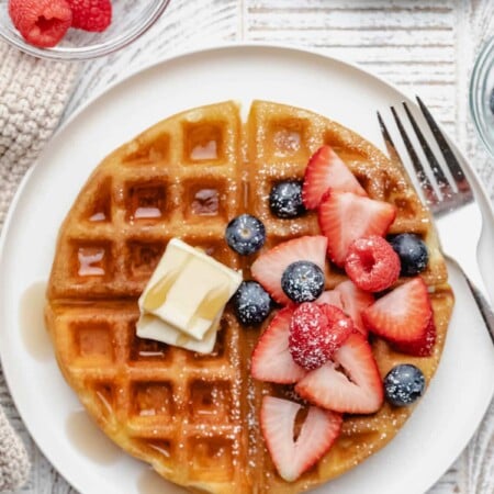 Buttermilk waffle topped with fresh berries and butter on a plate.
