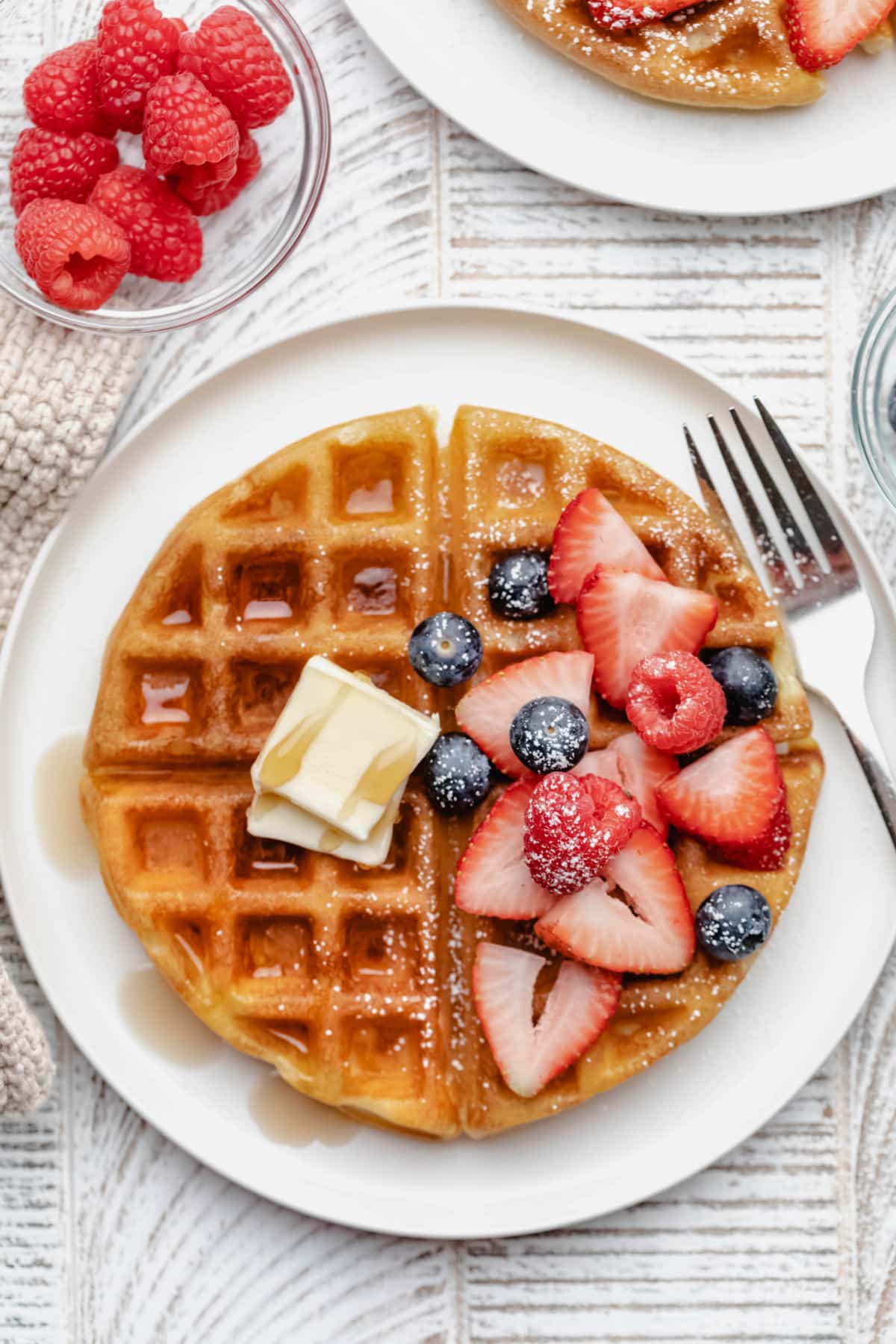 A buttermilk waffle topped with two pats of butter syrup and fresh berries. 