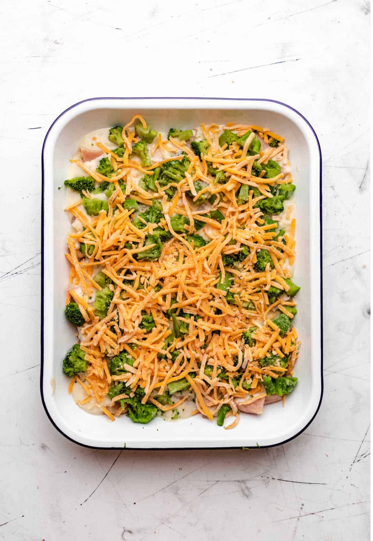 Shredded cheddar cheese over broccoli in a baking dish.