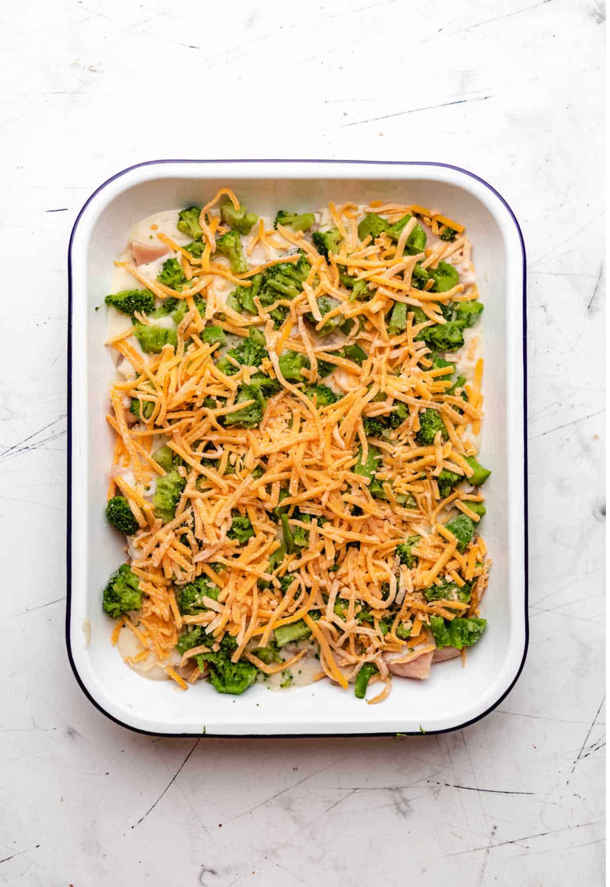 Shredded cheddar cheese over broccoli in a baking dish.