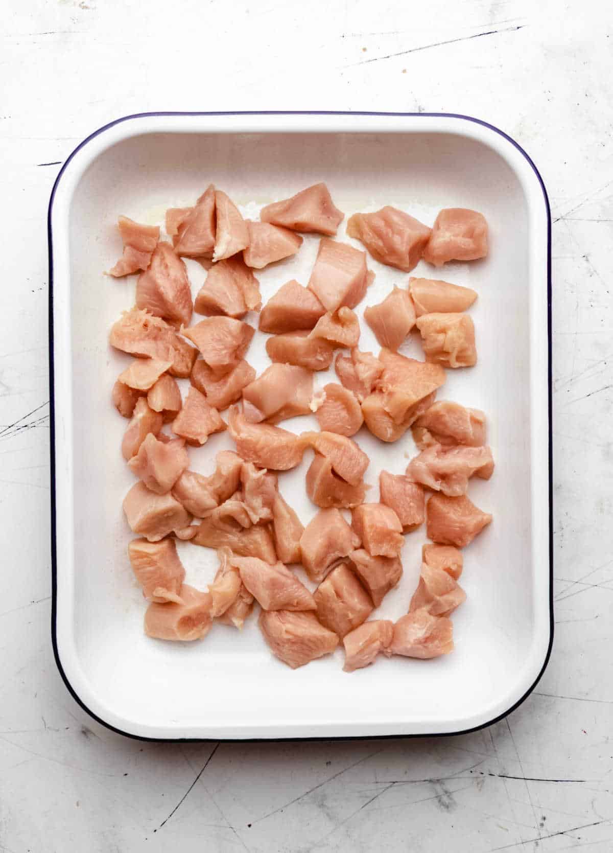 Pieces of raw chicken in a white baking dish.