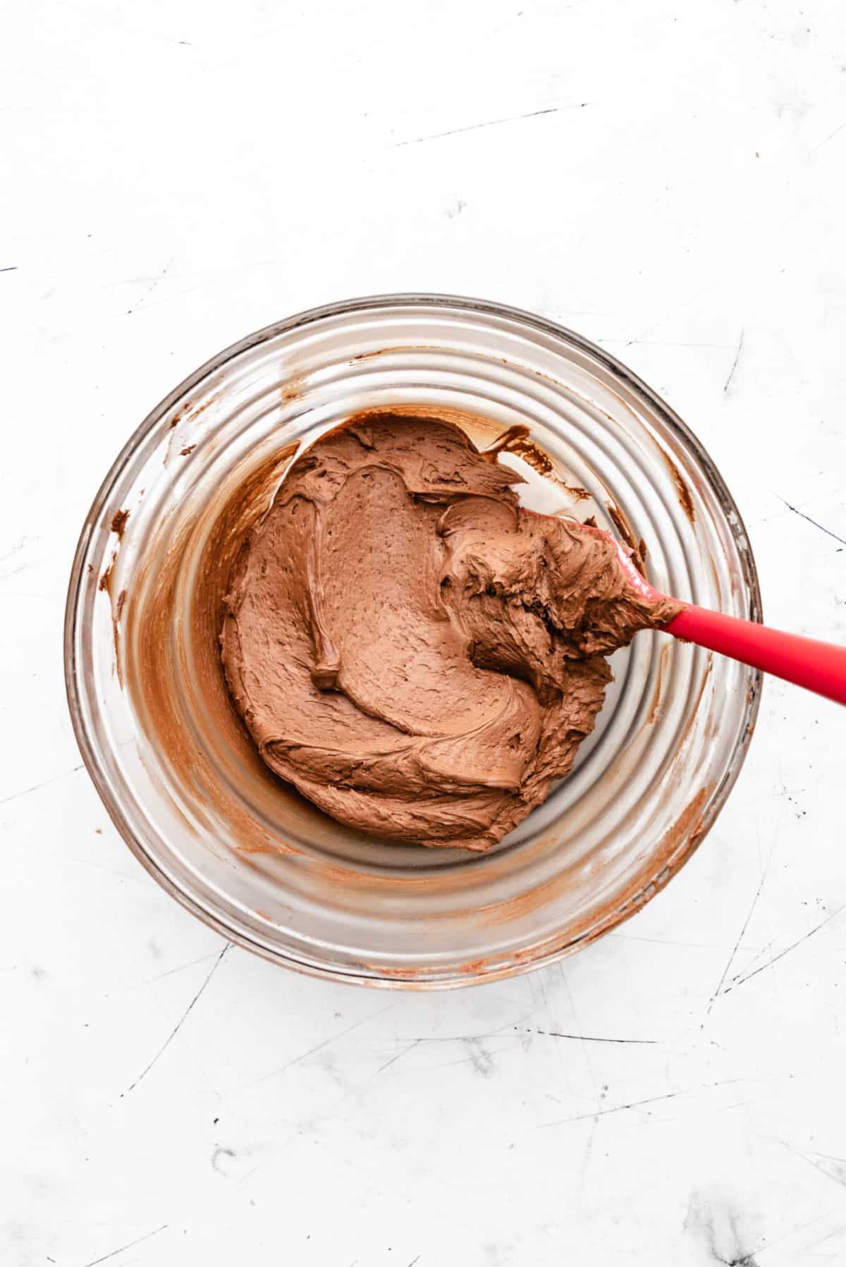 Chocolate buttercream frosting in a glass mixing bowl.