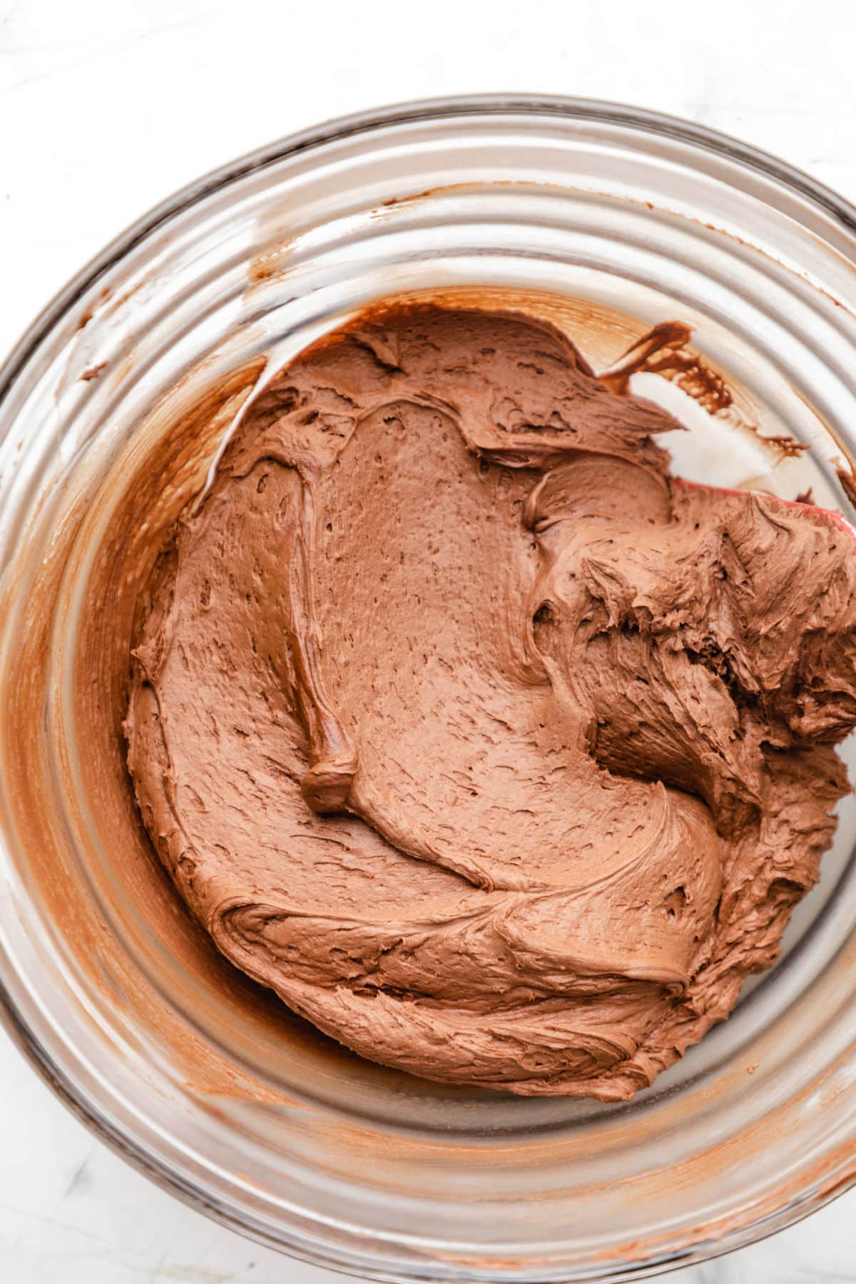 Close up photo of chocolate buttercream frosting in a glass mixing bowl.