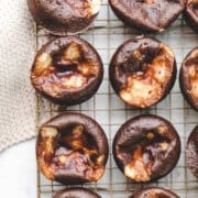 Two rows of chocolate cheesecake cupcakes on a wire cooling rack.