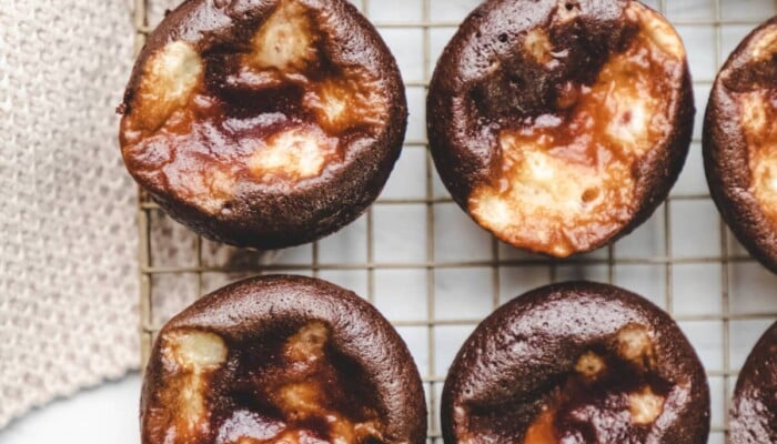 Two rows of chocolate cheesecake cupcakes on a wire cooling rack.