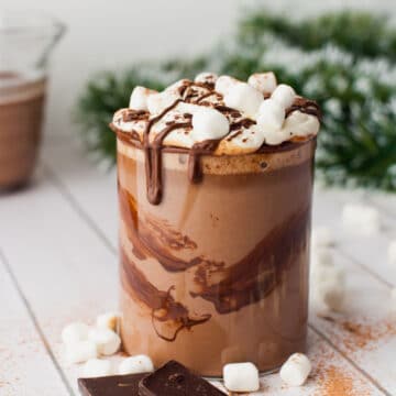 A glass of crock pot hot chocolate surrounded by chocolate bars and marshmallows.