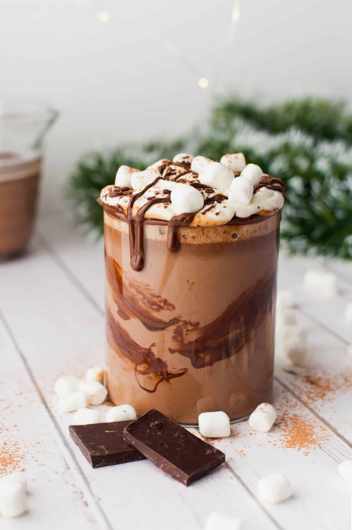 A glass of crock pot hot chocolate surrounded by chocolate bars and marshmallows. 