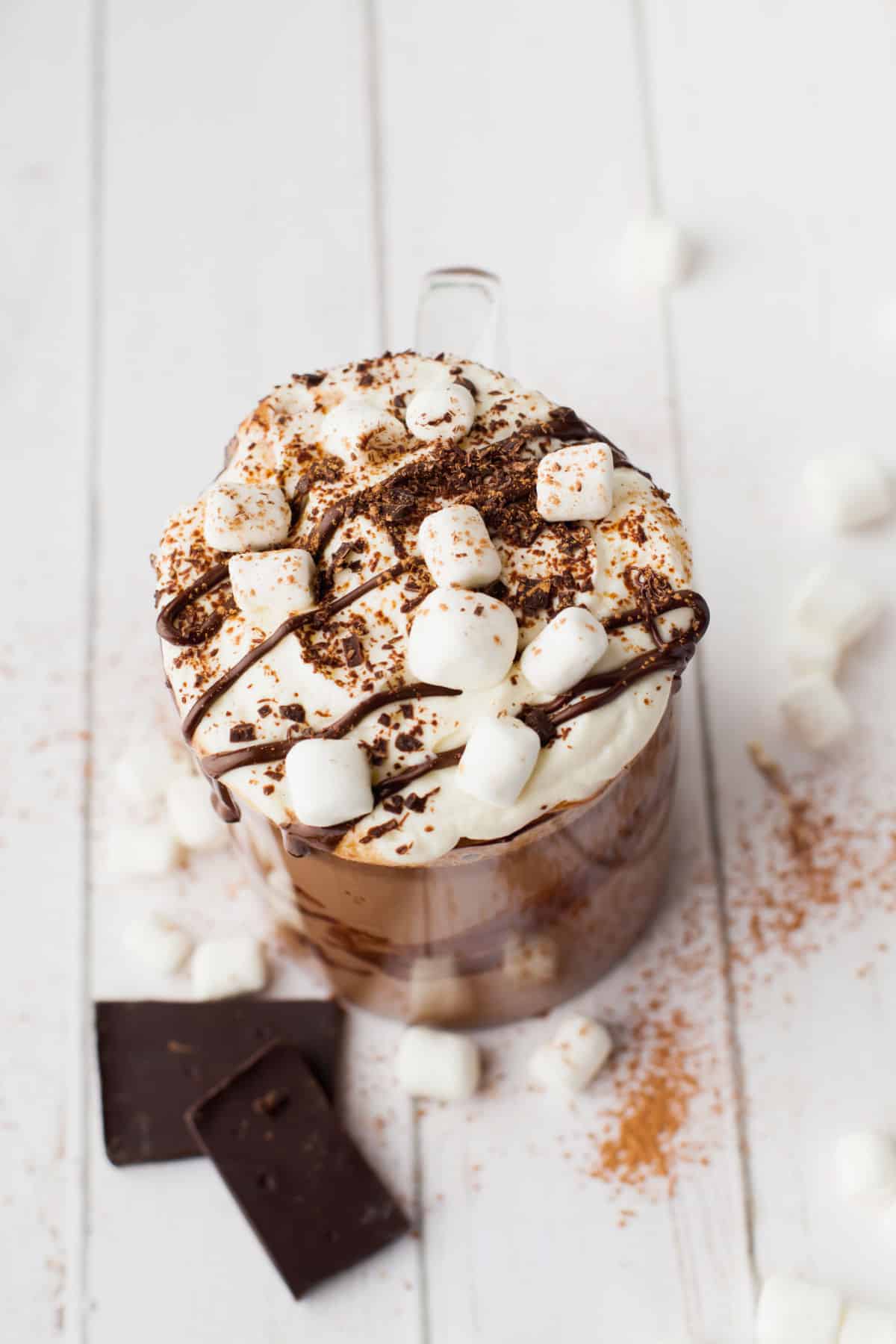 A mug of hot chocolate topped with marshmallows and a drizzle of chocolate syrup. 