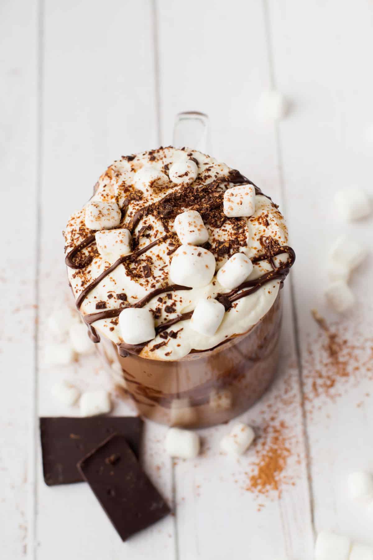 A mug of hot chocolate topped with marshmallows and a drizzle of chocolate syrup.