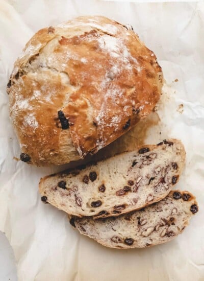 A loaf of no knead raisin bread with two slices cut.