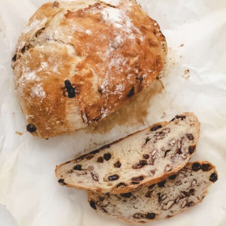 A loaf of no knead cinnamon raisin bread and two slices on a piece of parchment paper.