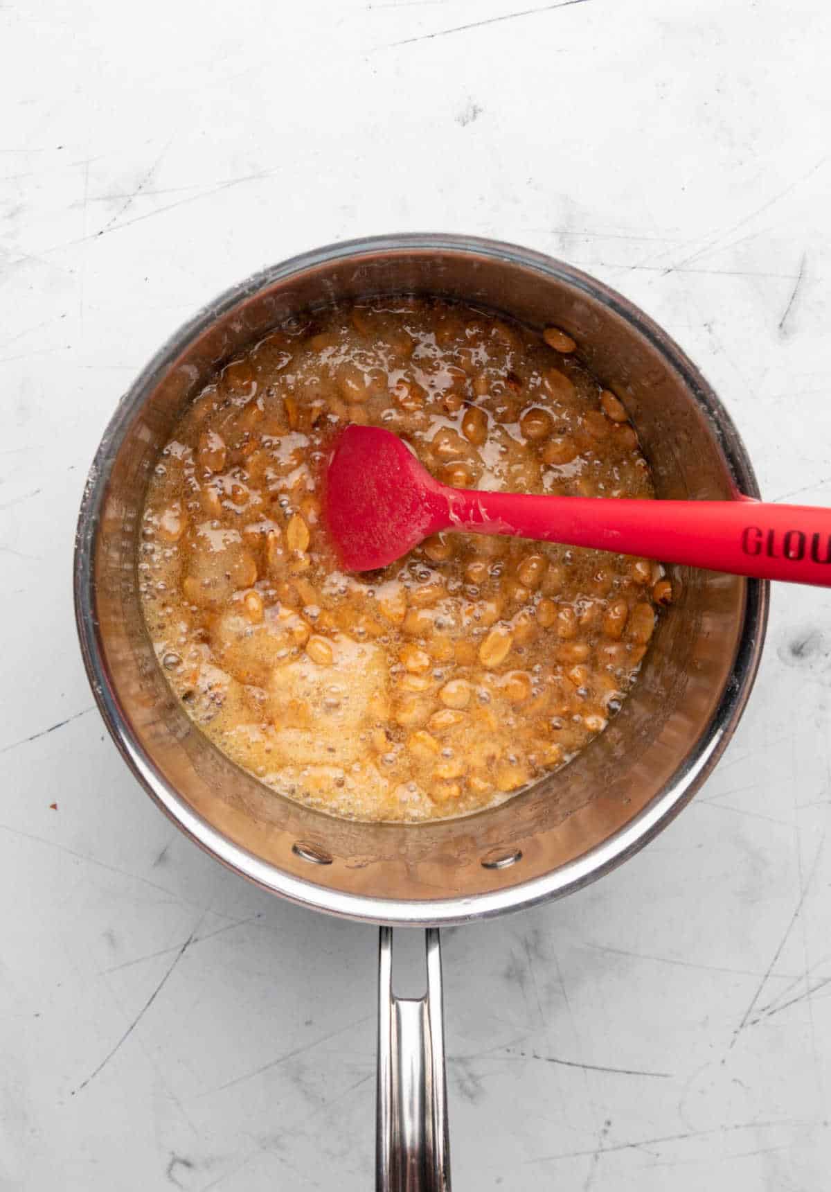 Amber colored peanut brittle mixture cooking in a saucepan. 
