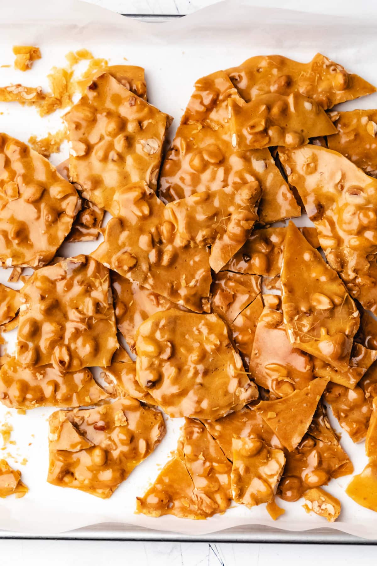 Pieces of peanut brittle piled up on a piece of parchment paper. 