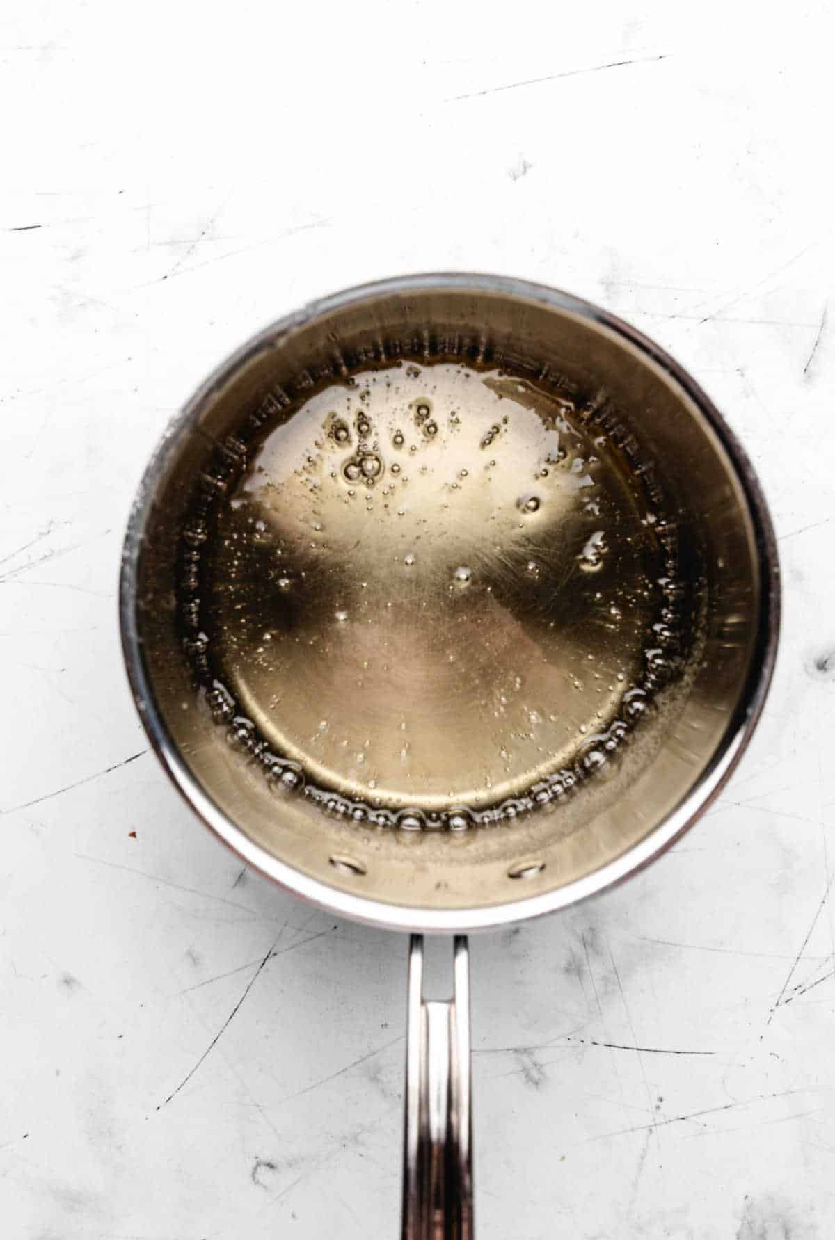 Corn syrup mixture coming to a boil in a saucepan.