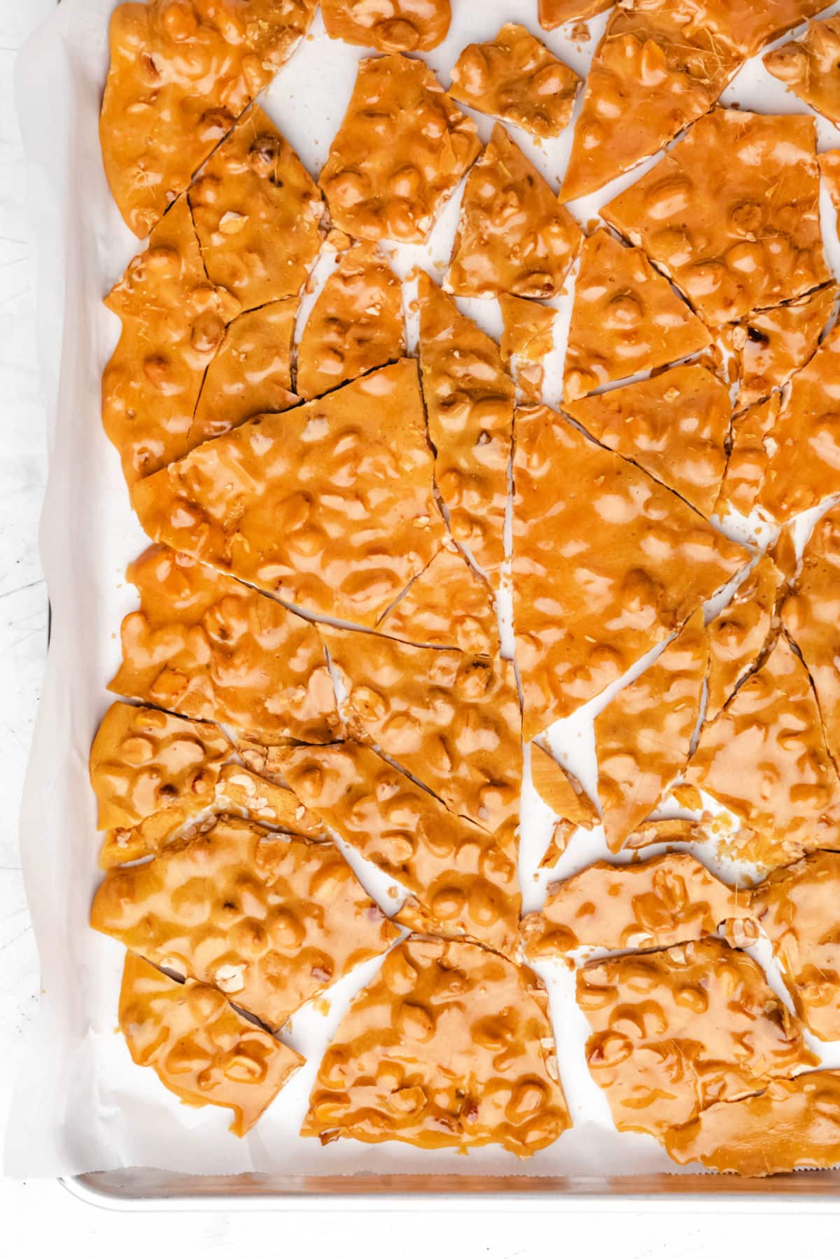 Broken pieces of peanut brittle on a baking tray. 