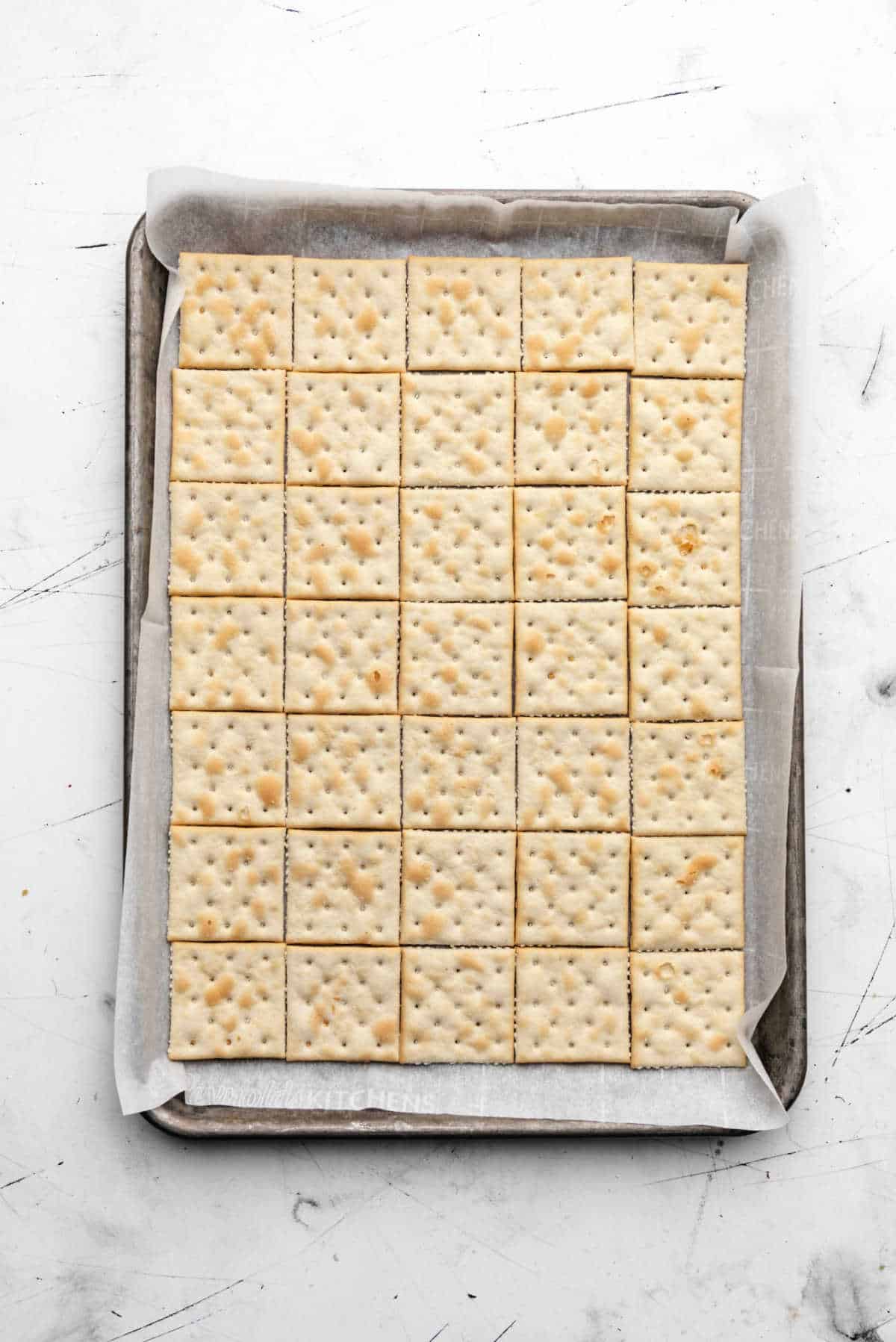 A jelly roll pan lined with parchment paper and topped with saltine crackers. 