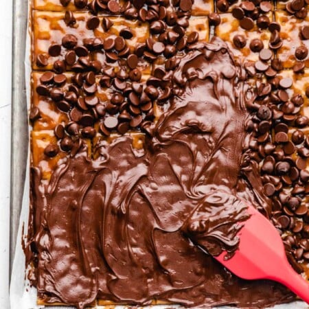 A red spatula spreading melted chocolate chips onto toffee.