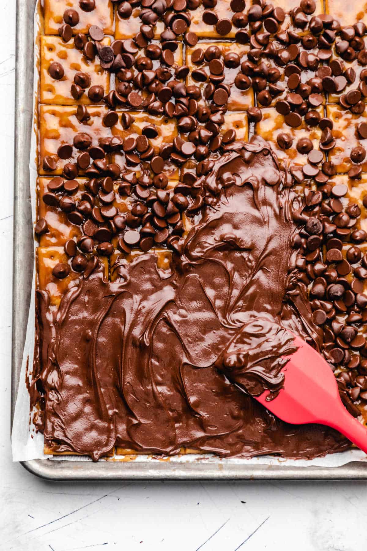 A red spatula spreading melted chocolate chips onto toffee. 