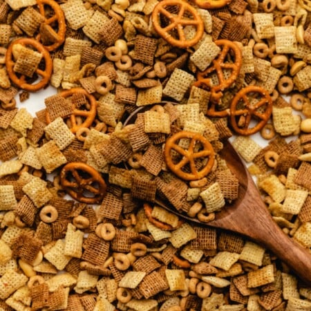 A wooden spoon scooping up slow cooker Chex mix from a baking tray.