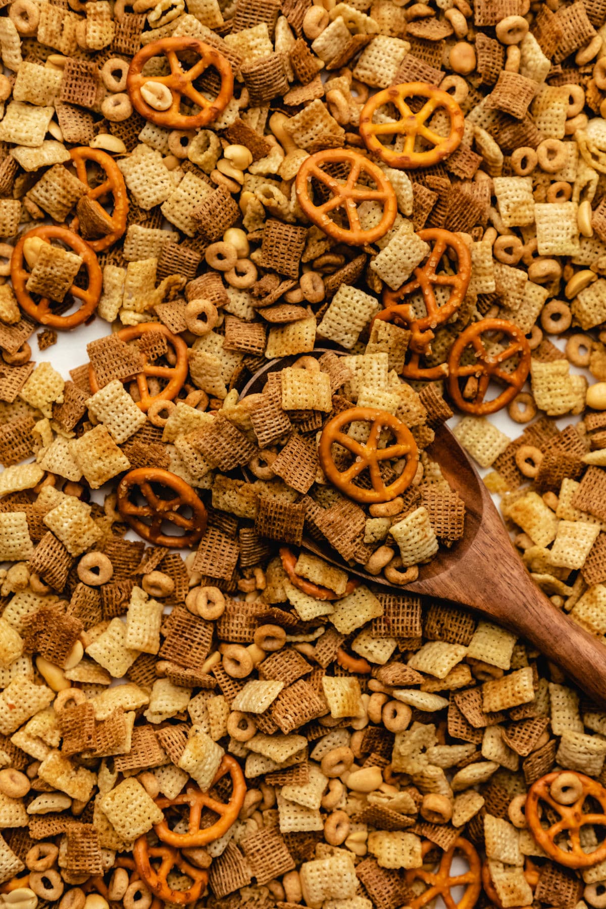A wooden spoon scooping up slow cooker Chex mix from a baking tray.