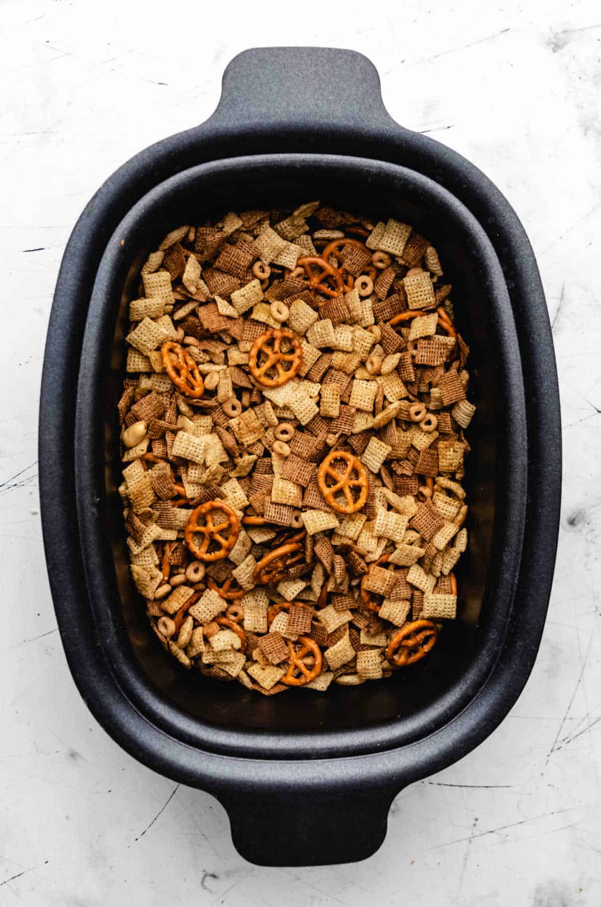 Cooked chex mix in a slow cooker insert. 