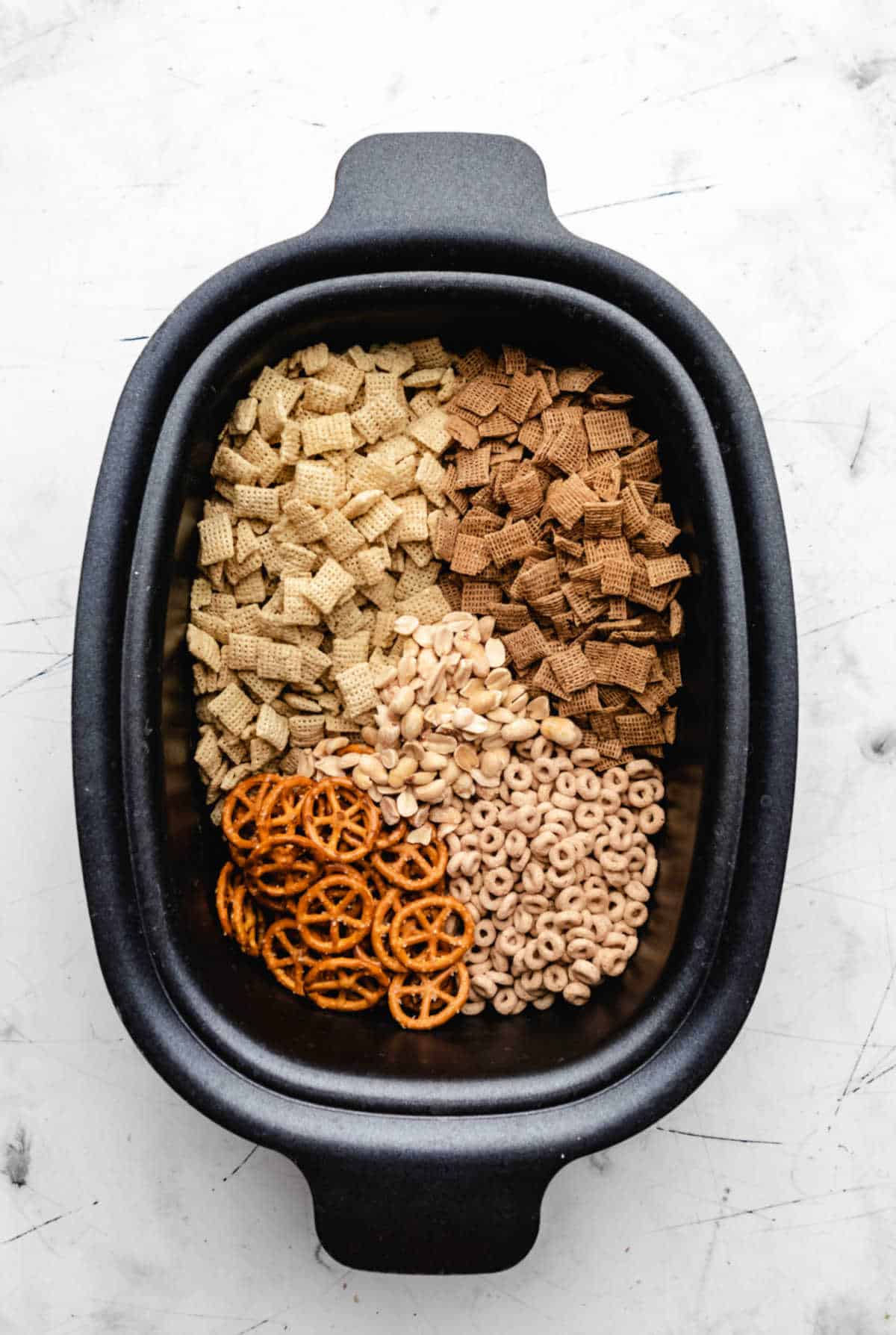 Cereal pretzels and nuts in a slow cooker insert. 