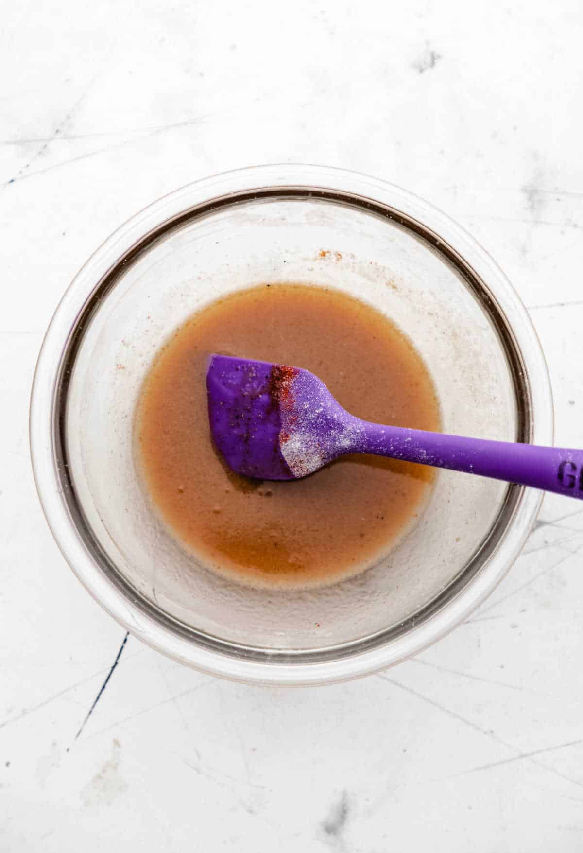 A purple spatula in a butter and spice mixture. 