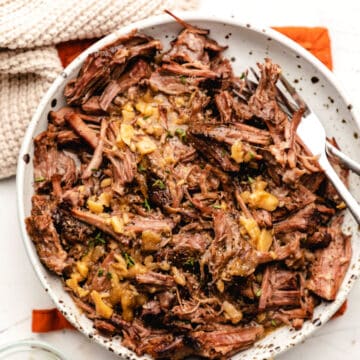 A plate of crock pot garlic pot roast on an orange pot holder.