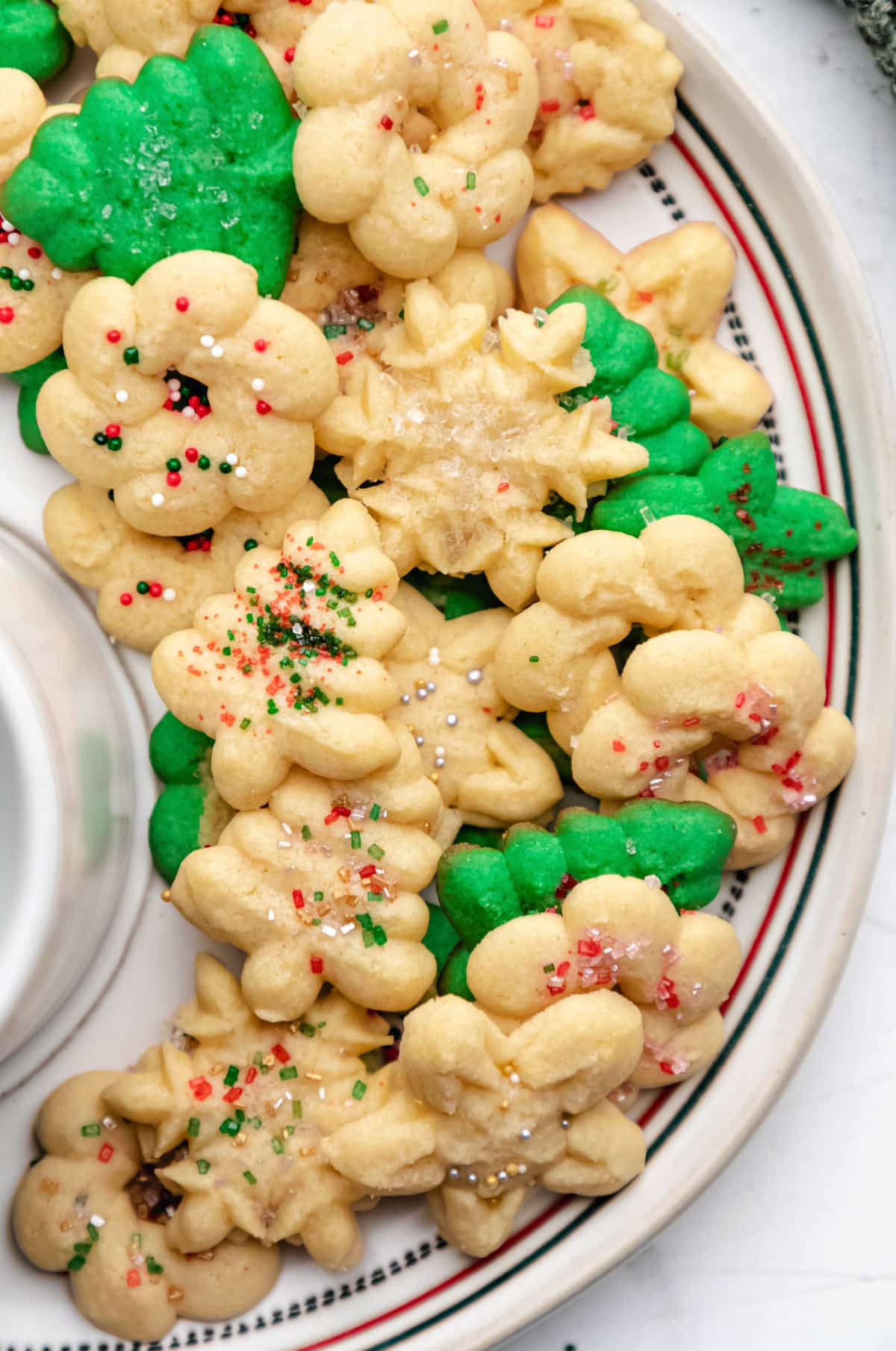 A close up photo of white and green spritz cookies on a white plate. 