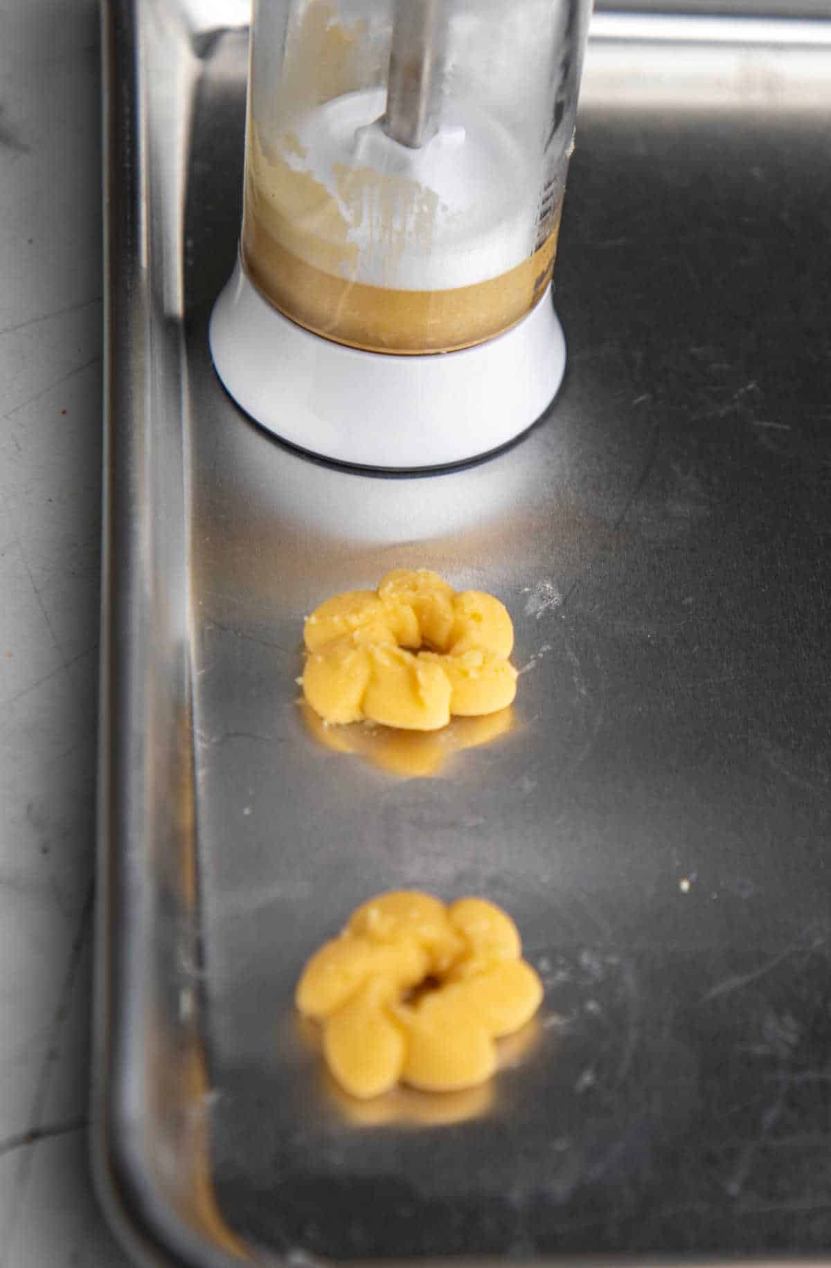 A cookie press pressing dough onto a cookie sheet. 