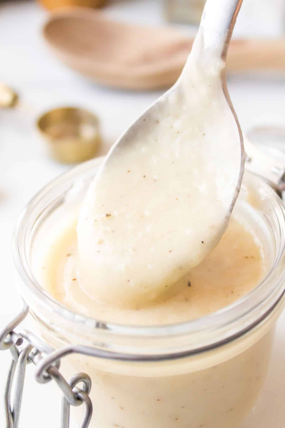 A spoon scooping cream of chicken substitute out of a glass jar. 