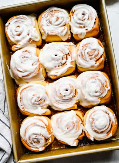 A dozen honey buns with frosting in a pan.